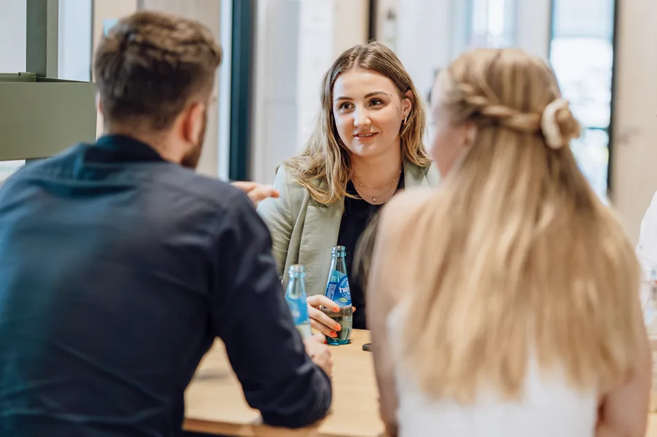 Three people sitting at a table having a conversation, with one woman holding a bottle of water.