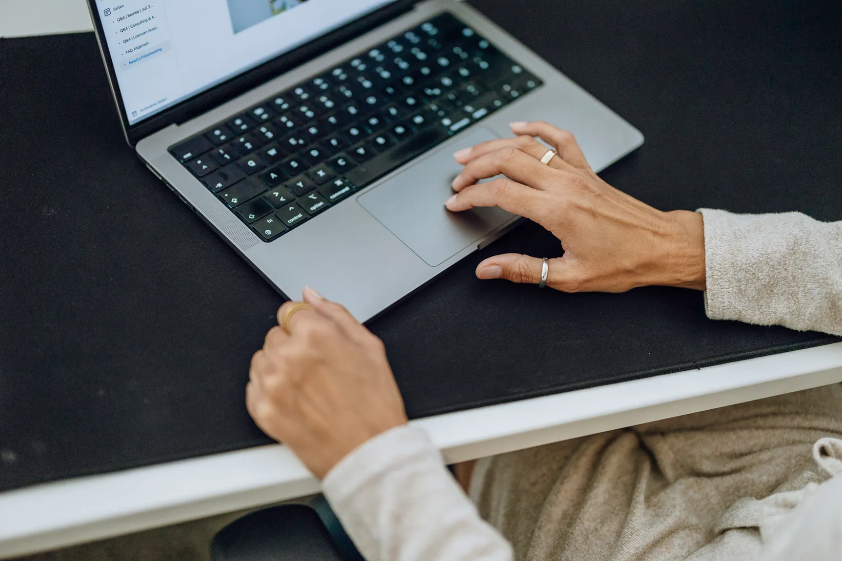 Close-up of hands typing on a laptop keyboard, with a focus on the touchpad and screen displaying a document.