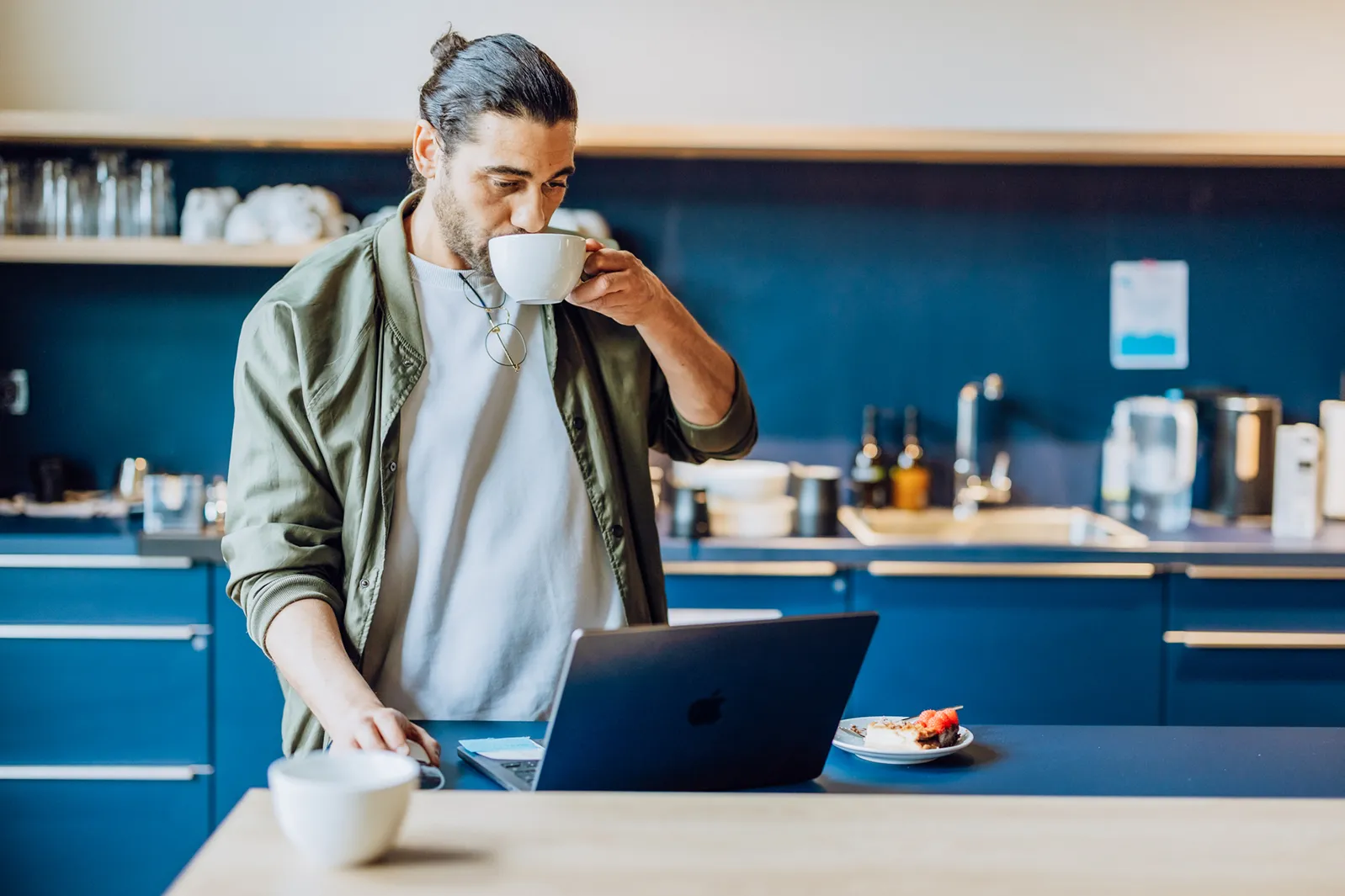 Man drinking coffee while using a laptop in a modern kitchen setting.