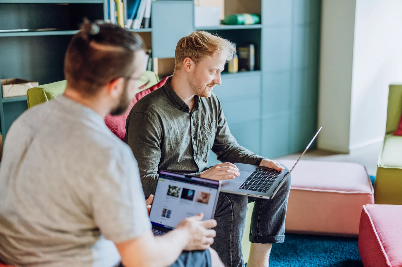 Two men sitting on colorful furniture, using laptops in a modern office setting.