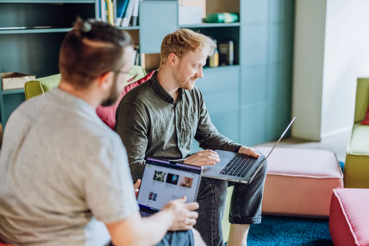 Two men sitting on colorful furniture, using laptops in a modern office setting.