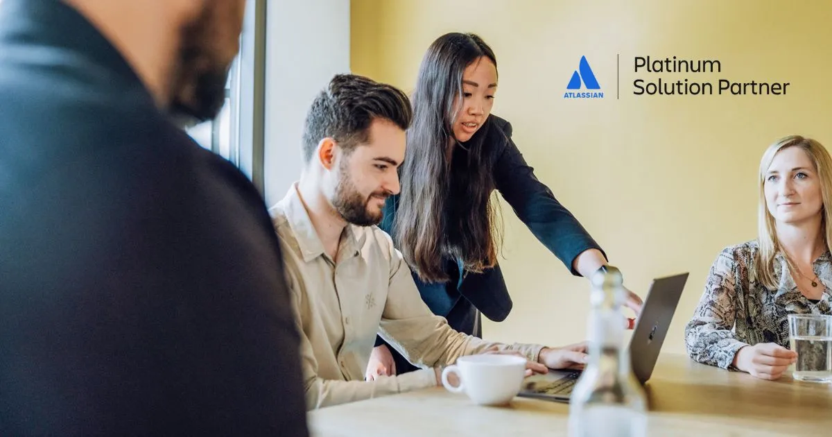 Two women and a man in an office setting, with one woman pointing at a laptop screen while others observe. The Atlassian Platinum Solution Partner logo is in the upper right corner.